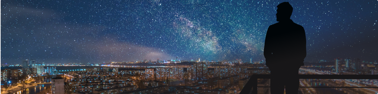 Homem olhando o orizonte com uma cidade iluminada e o céu estrelado